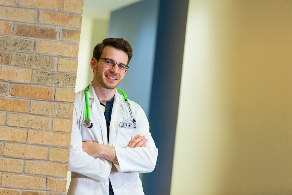 Nurse with stethoscope on neck leaning against a wall