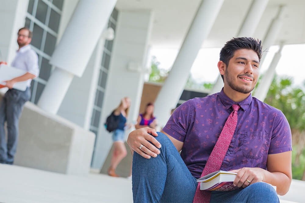 male student with book on steps of special event center